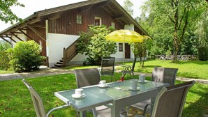 A glass table with chairs and a yellow umbrella in a garden setting. - Vacation Apartment "Bayerwaldtraum" with Pool and Wi-Fi (Hauzenberg)