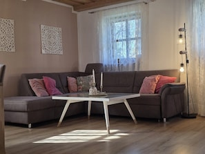 A modern living room with a grey sectional sofa, a white coffee table, decorative wall art, and a floor lamp. - Vacation Apartment "Bayerwaldtraum" with Pool and Wi-Fi (Hauzenberg)