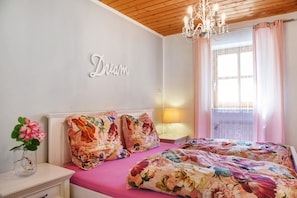 A bedroom with a floral bedspread, a bedside table with a lamp, a wall-mounted word 'Dream,' and a window with curtains. - Vacation Apartment "Bayerwaldtraum" with Pool and Wi-Fi (Hauzenberg)