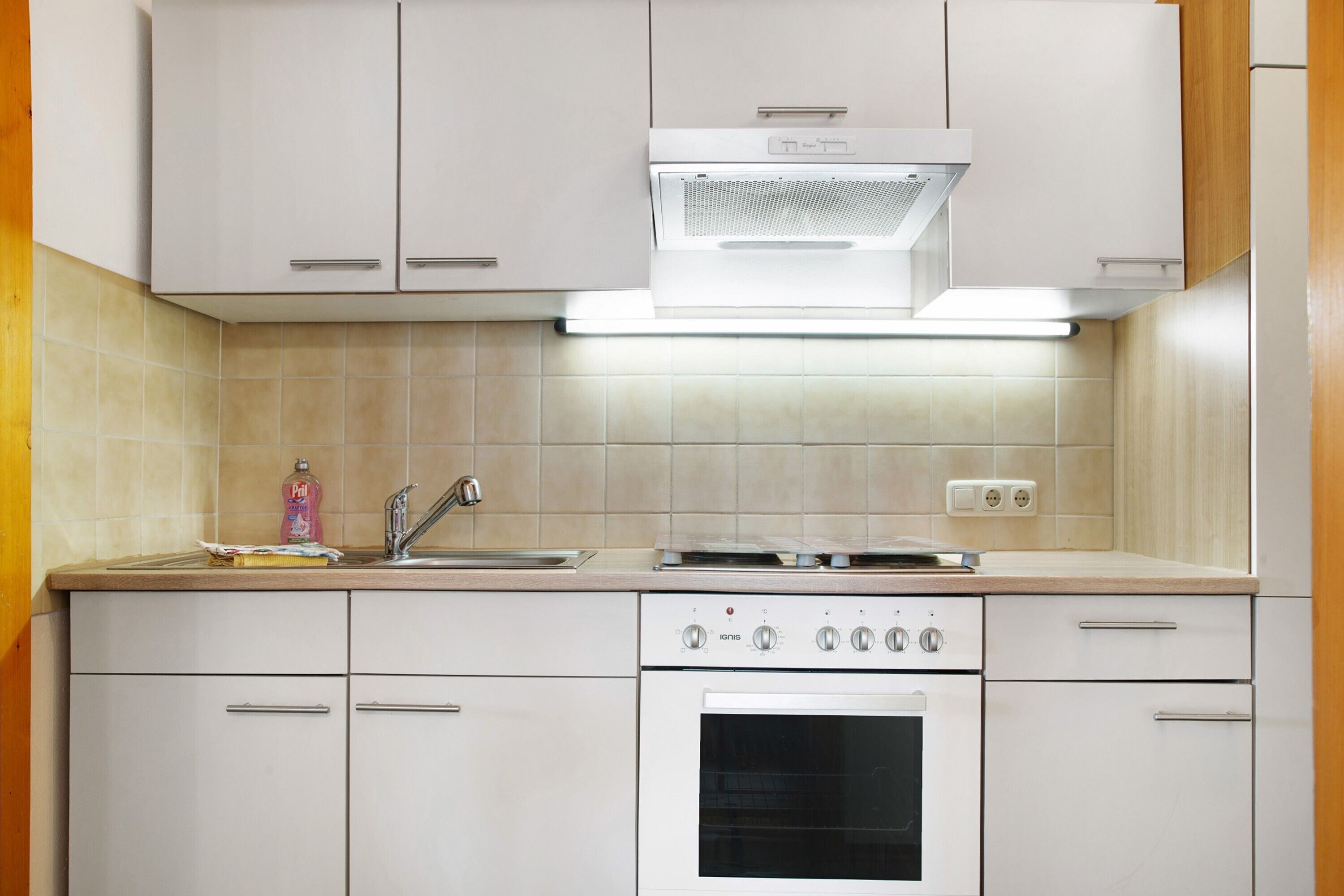 A kitchen with white cabinets, a stove, an oven, a sink, and a range hood.