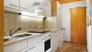 A compact kitchen with a sink, stove, oven, and wooden cabinets. - Vacation Apartment "Bayerwaldtraum" with Pool and Wi-Fi (Hauzenberg)