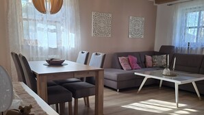A living room with a wooden ceiling, a dining table with chairs, a sofa, a coffee table, and decorative wall art. - Vacation Apartment "Bayerwaldtraum" with Pool and Wi-Fi (Hauzenberg)