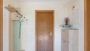 Un pasillo con una puerta de madera, un perchero, un pequeño estante con flores y un armario.