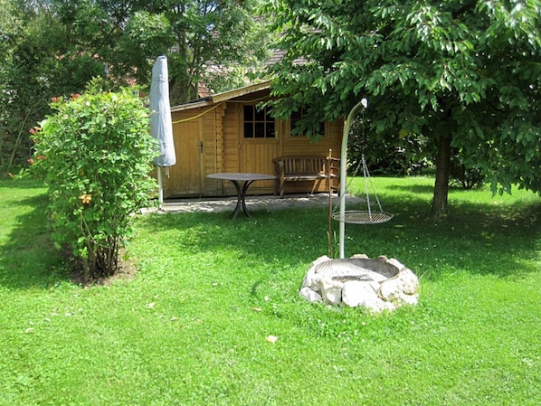 Una cabaña de madera con una mesa y un banco en un patio cubierto de césped.