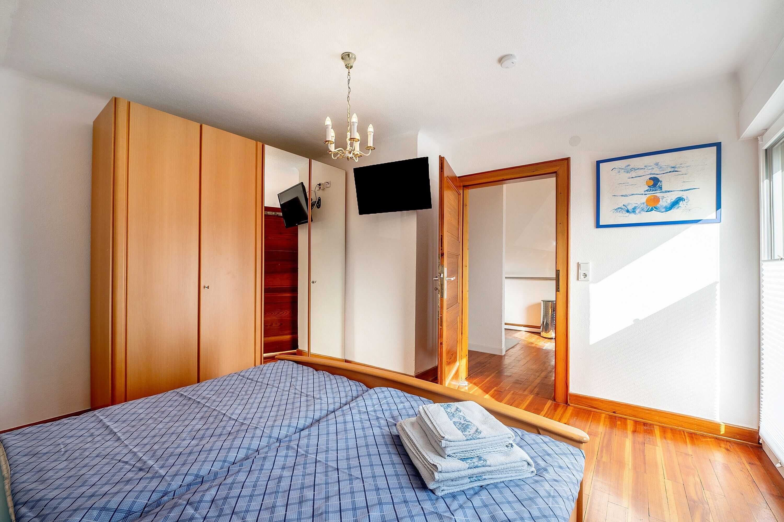 A bedroom with a bed, wooden wardrobe, a television, and a framed picture on the wall.