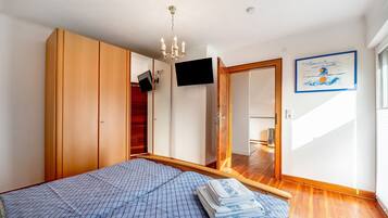 A bedroom with a bed, wooden wardrobe, a television, and a framed picture on the wall.