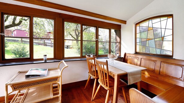 A dining area with a table, chairs, and a bench. There are large windows with a view of greenery outside. - Holiday Home 'Domäne Bollinger Morbach' with Private Terrace, Private Garden and Wi-Fi (Morbach)