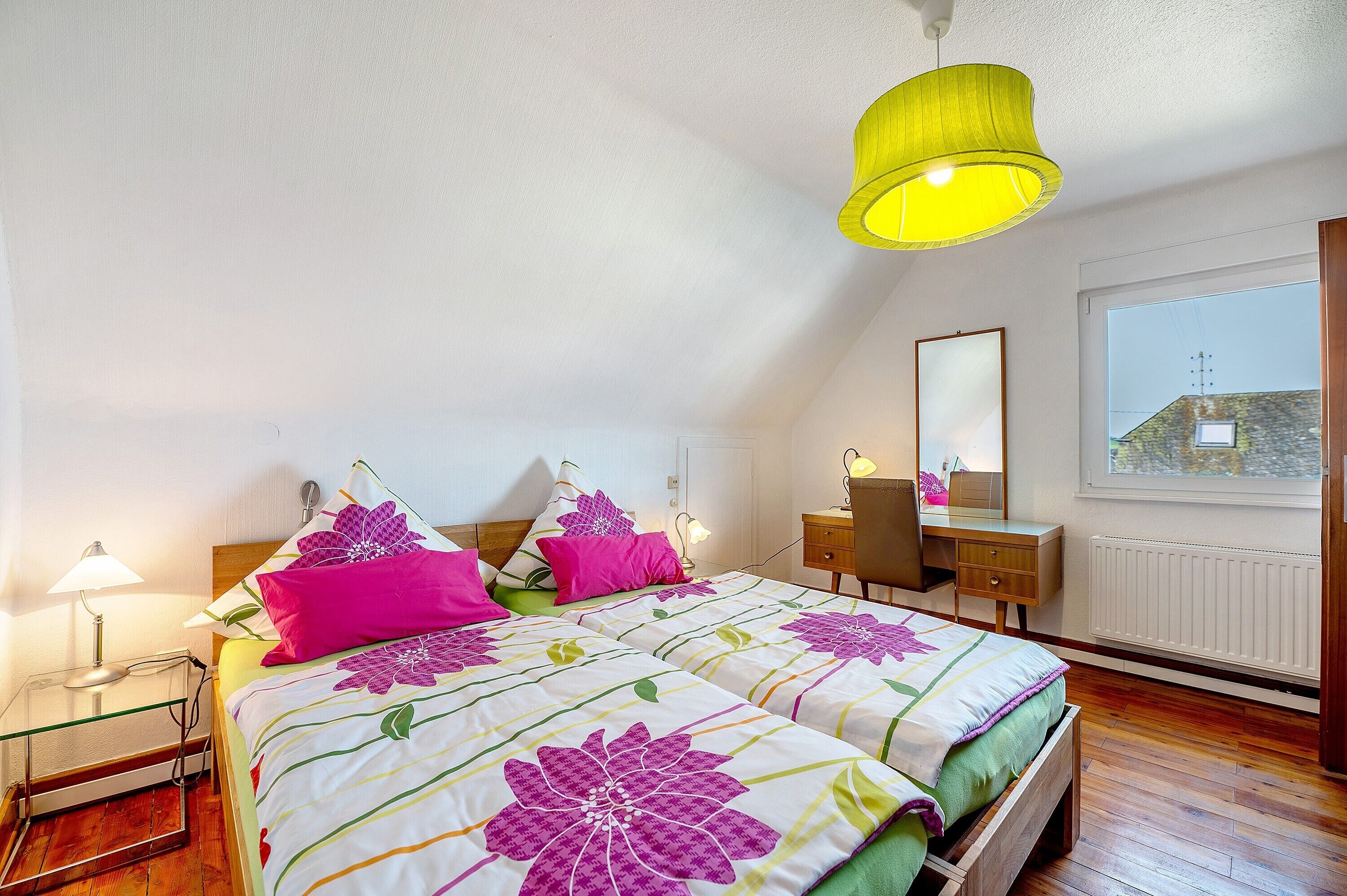 A bedroom with a bed, bedside lamps, a desk, and a window.