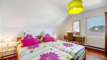 A bedroom with a bed, bedside lamps, a desk, and a window.