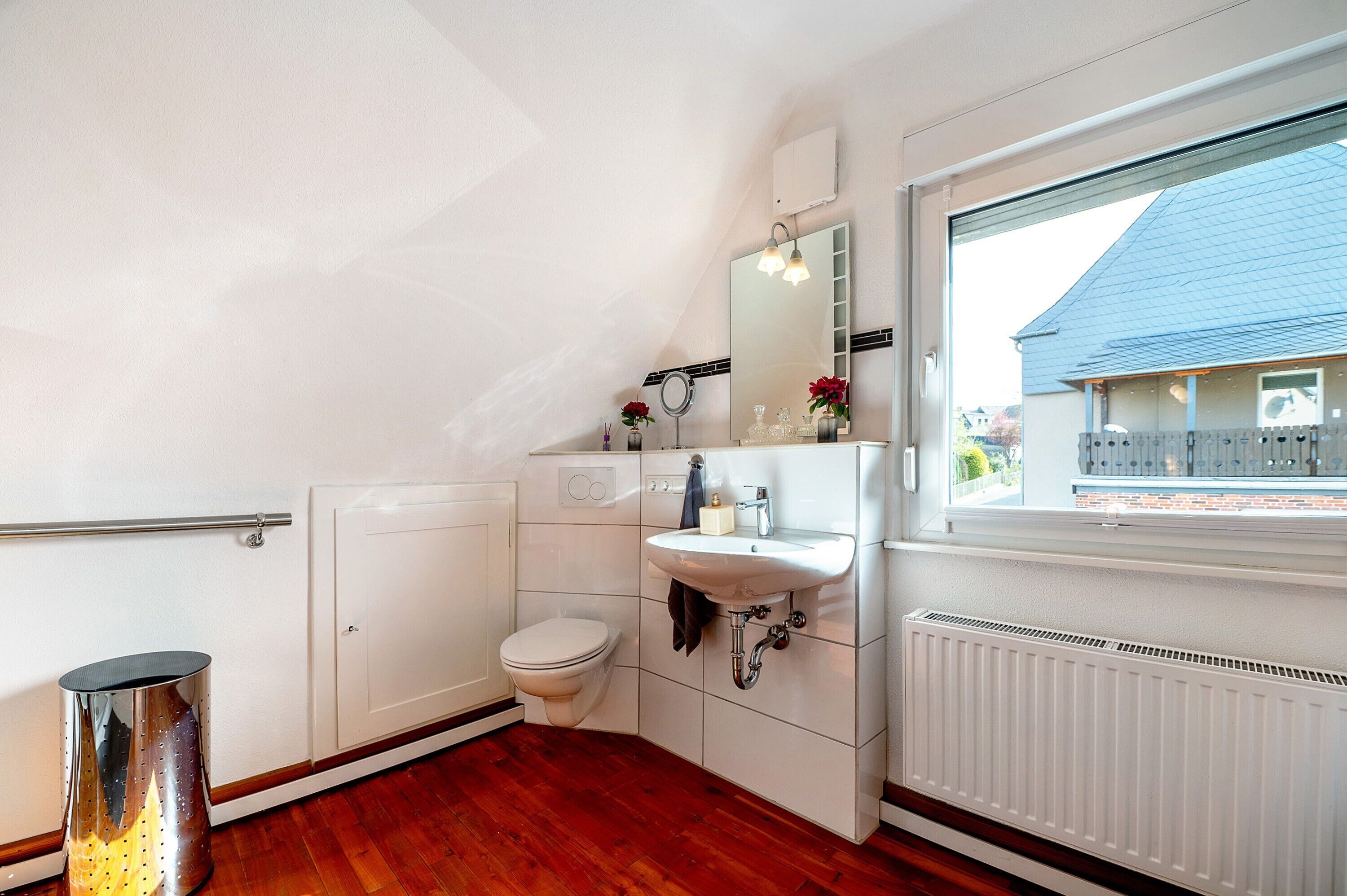 A bathroom with a toilet, sink, mirror, and window.