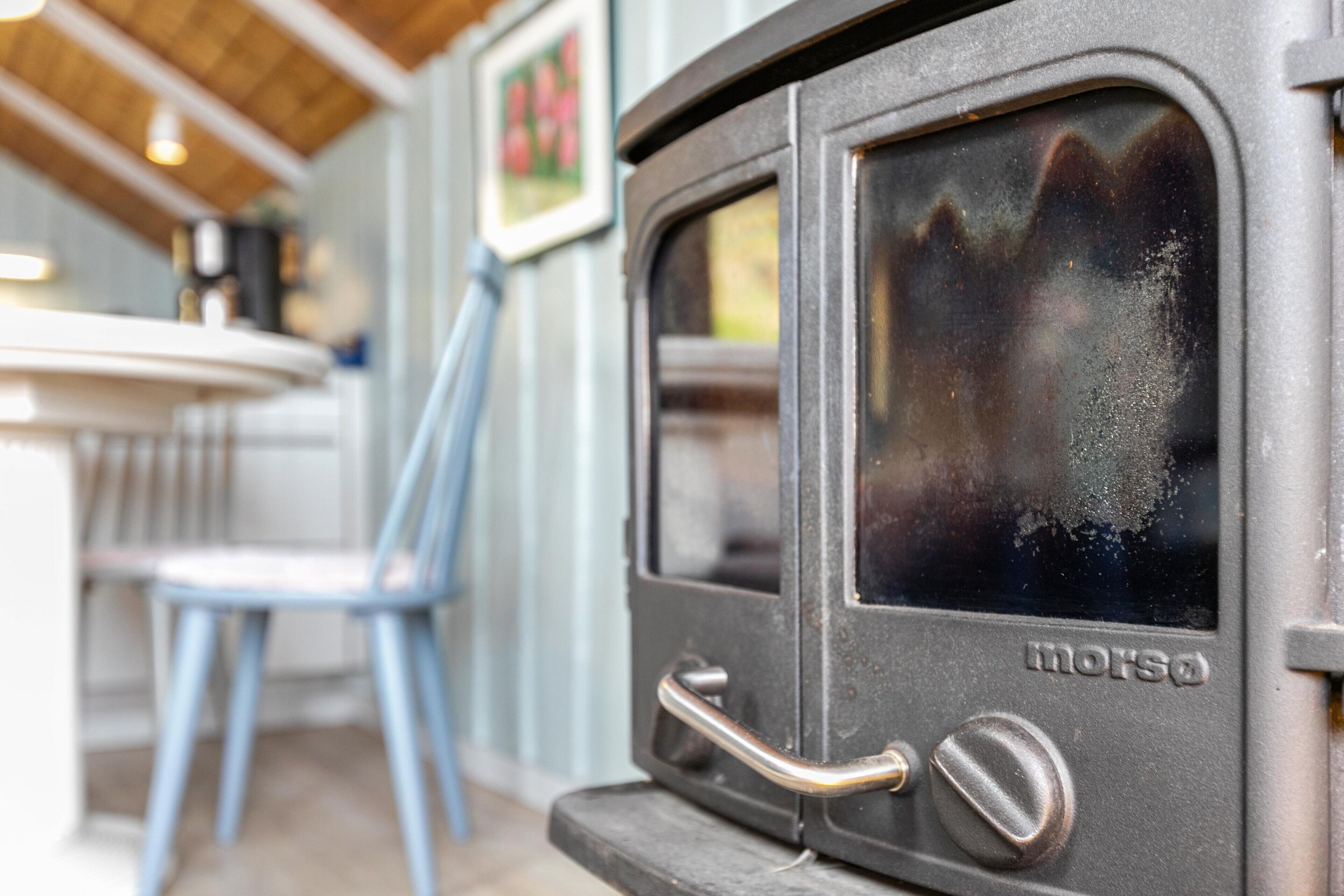 A vintage stove with a handle and knob, a blue chair, and a table in the background.
