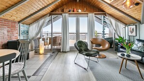 Tyylikäs huone, jossa on avoin pohjaratkaisu, viistokatto, suuret ikkunat, ruokailutila ja oleskelualue, josta on kaunis näköala.