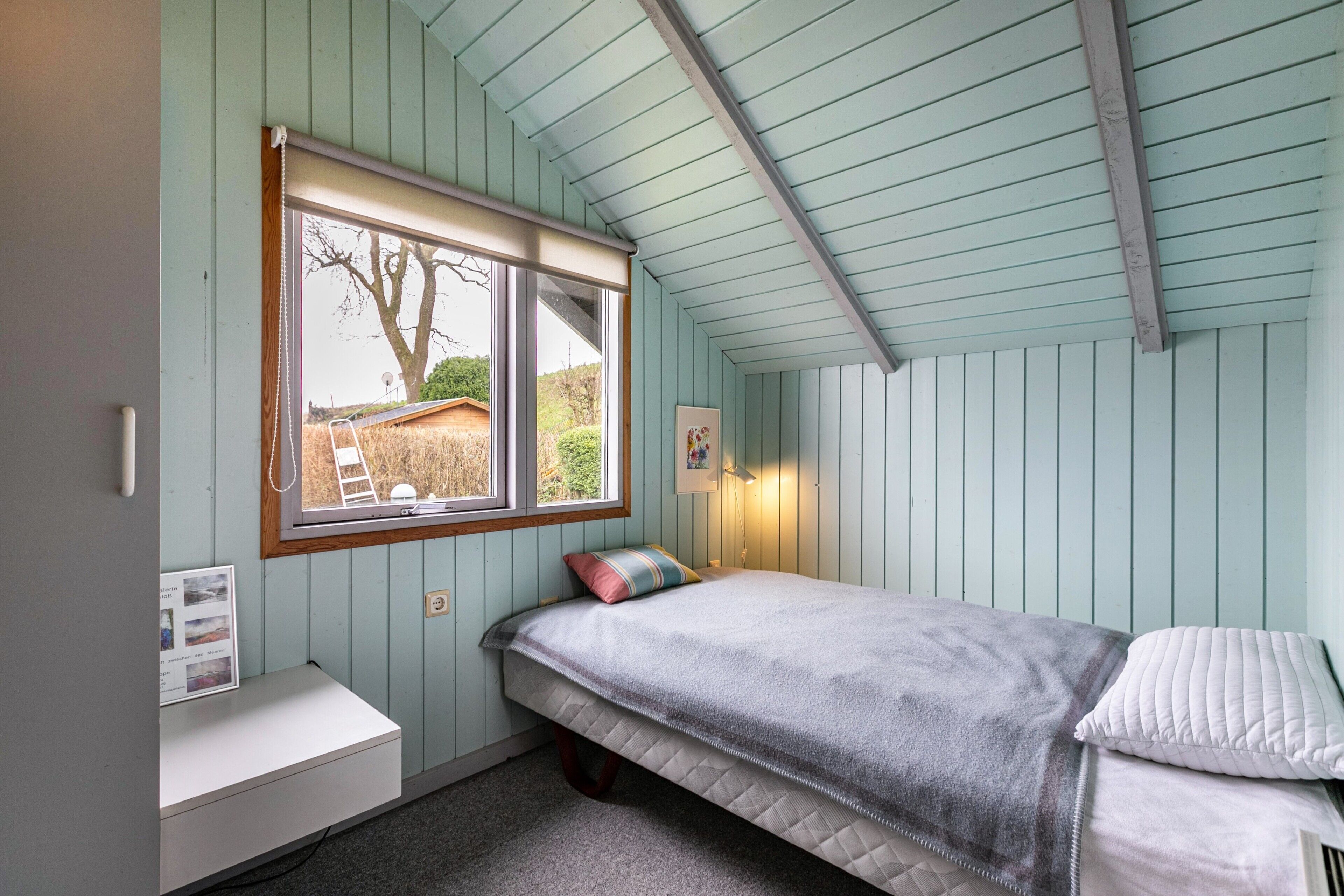 Un dormitorio con una cama individual, una ventana, un escritorio pequeño y una lámpara fijada a la pared.