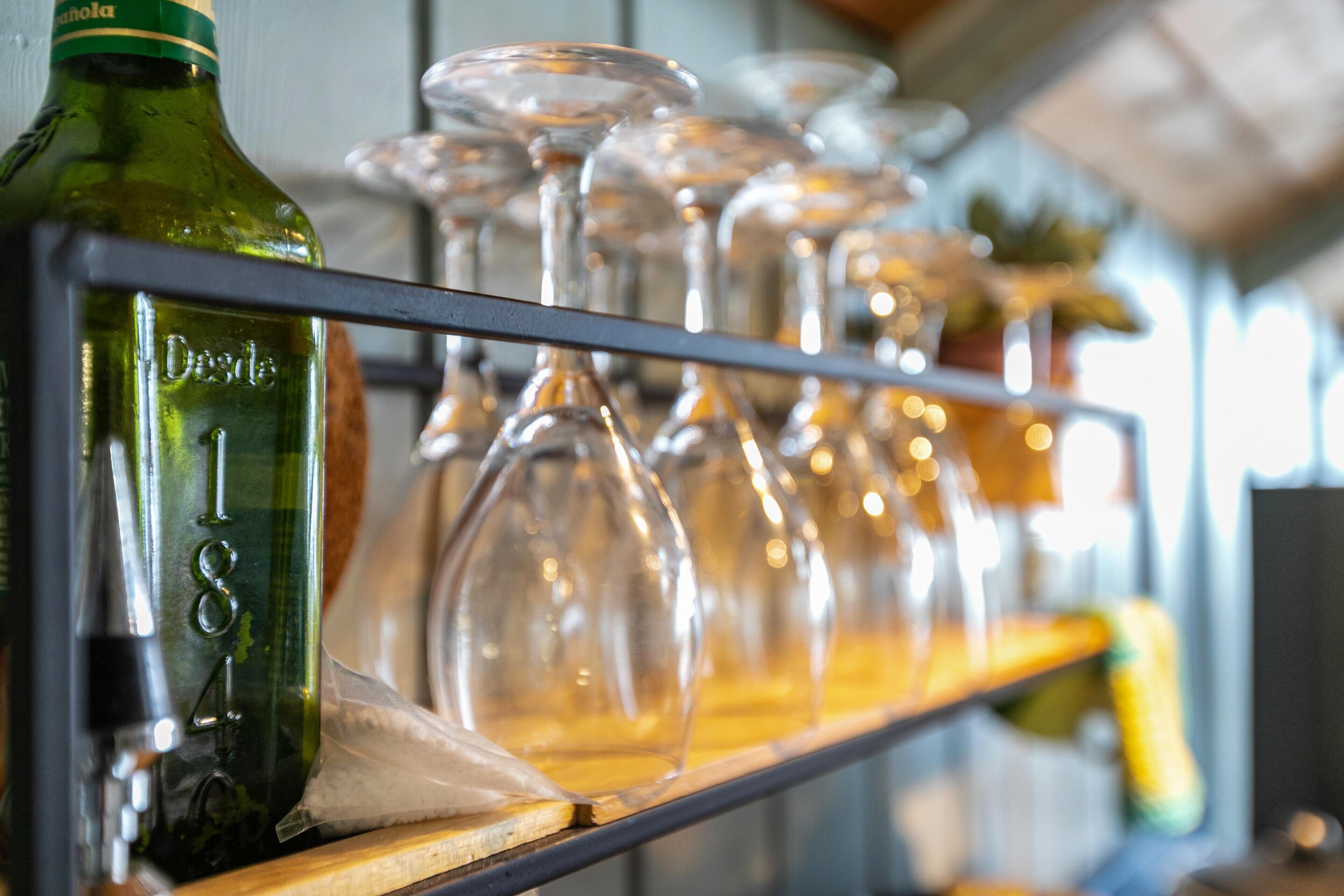 Una estantería con una botella verde etiquetada 'Desdel' y varios vasos de vino transparentes.