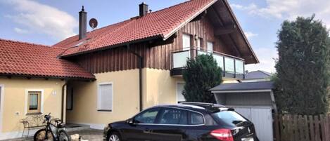 A house with a car parked in front, a bicycle, and a wooden fence.