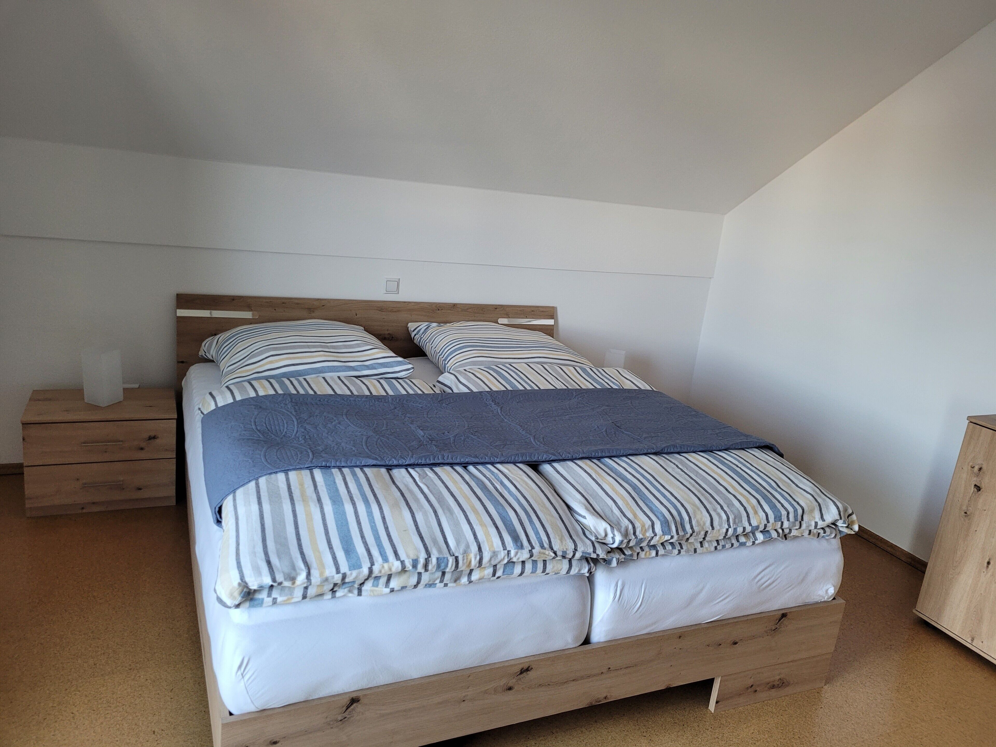 Ein Einzelbett mit Holzbettrahmen, zwei Nachttische und eine schlichte weiße Wand.