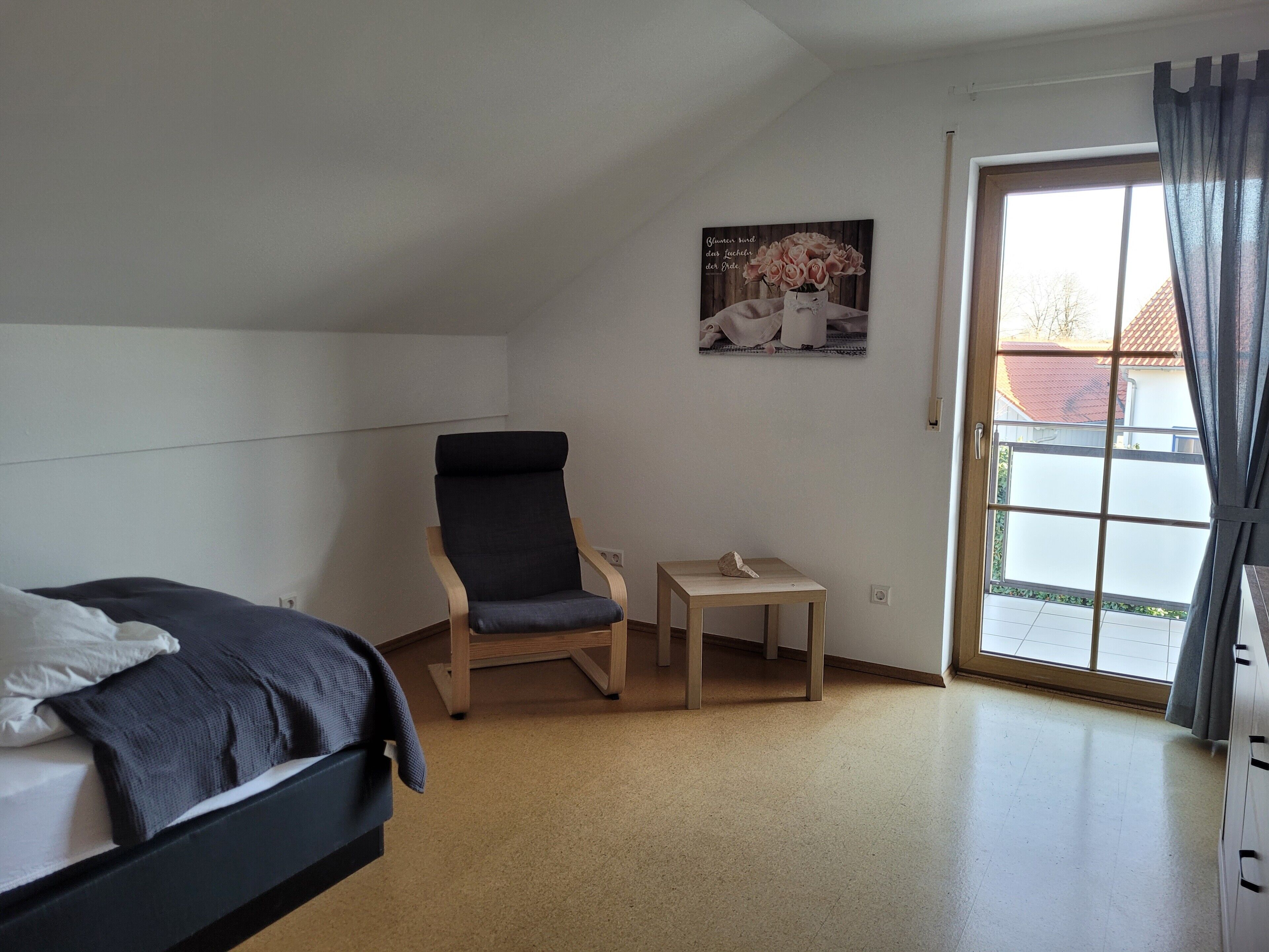 A bedroom with a bed, a chair, a small table, and a window with curtains.