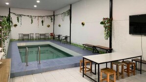A pool area with a rectangular pool, surrounded by seating and tables, and decorated with hanging plants. - Rakchayanin Resort Koh Larn (Koh Lan)