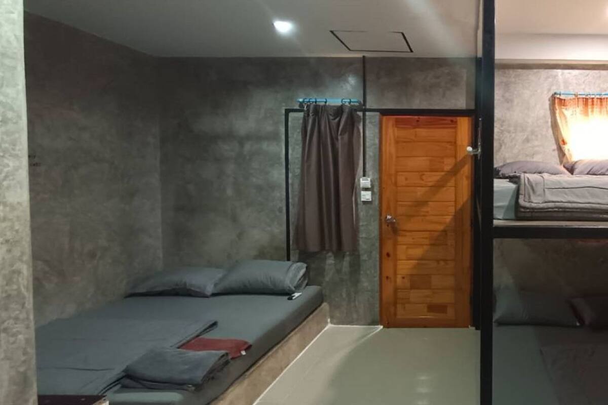 A compact bedroom with a single bed, a wooden door, and a small window with curtains.