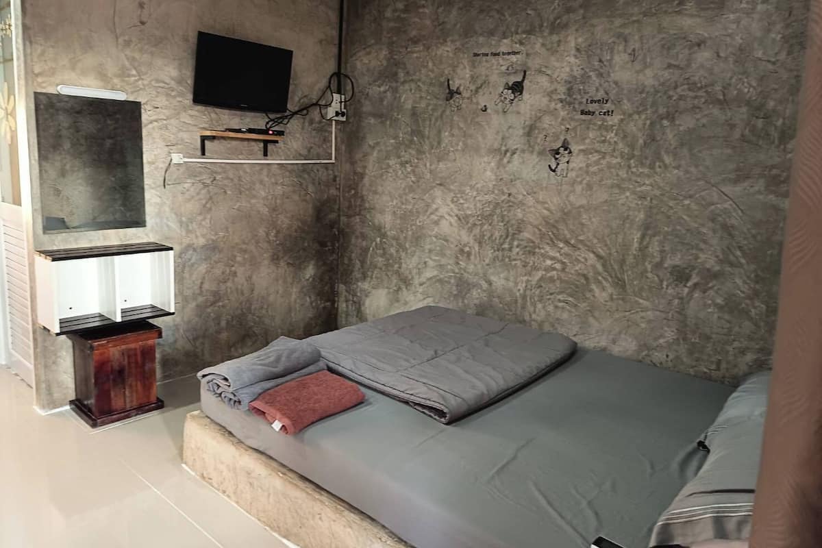 A bedroom with a bed, a TV mounted on the wall, and a small shelf.