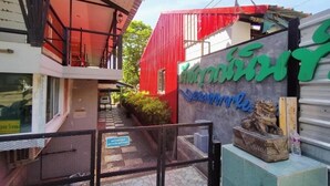 A building entrance with a red facade and a sign with green and blue text. - Rakchayanin Resort Koh Larn (Koh Lan)