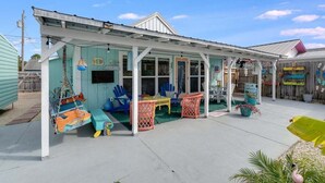 Un espacio al aire libre techado con sillas y mesas de colores, una pequeña zona de juegos con un columpio y una estatua decorativa de flamenco.