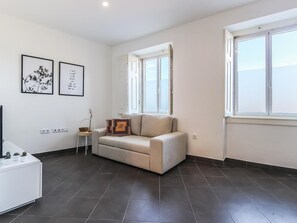 Un salon moderne avec un canapé, une petite table d’appoint, un téléviseur et une fenêtre donnant sur un beau paysage.