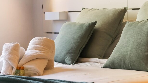 Una cama bien hecha con almohadas verdes y blancas, una toalla blanca doblada y una manta verde.
