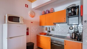 A compact kitchen with white appliances, orange cabinets, and a tiled backsplash.