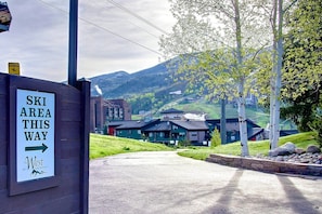 A sign indicating the direction to the ski area, with a view of buildings and a mountainous landscape in the background.