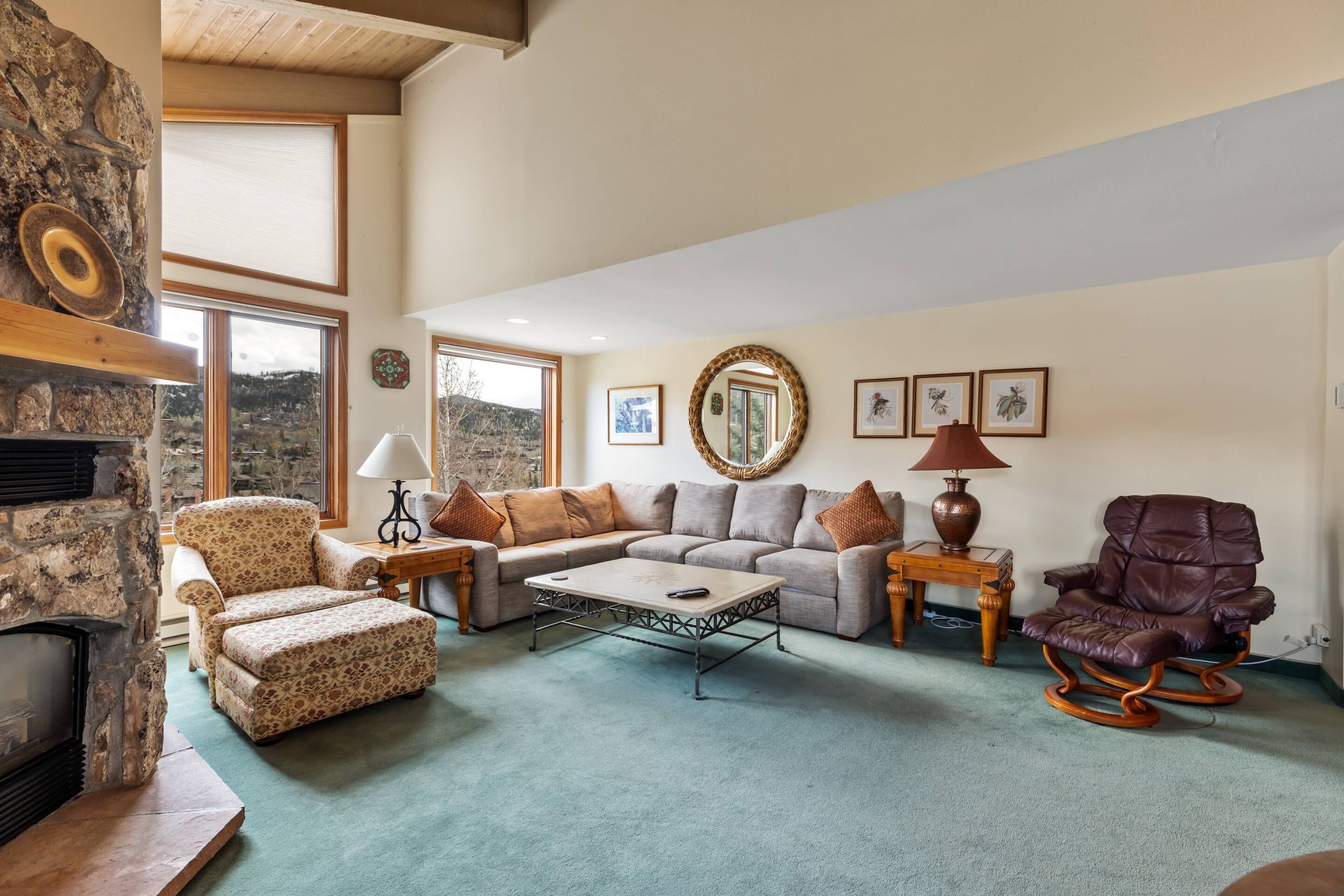 A spacious living room with a stone fireplace, a sectional sofa, a patterned armchair, a rocking chair, and a coffee table.