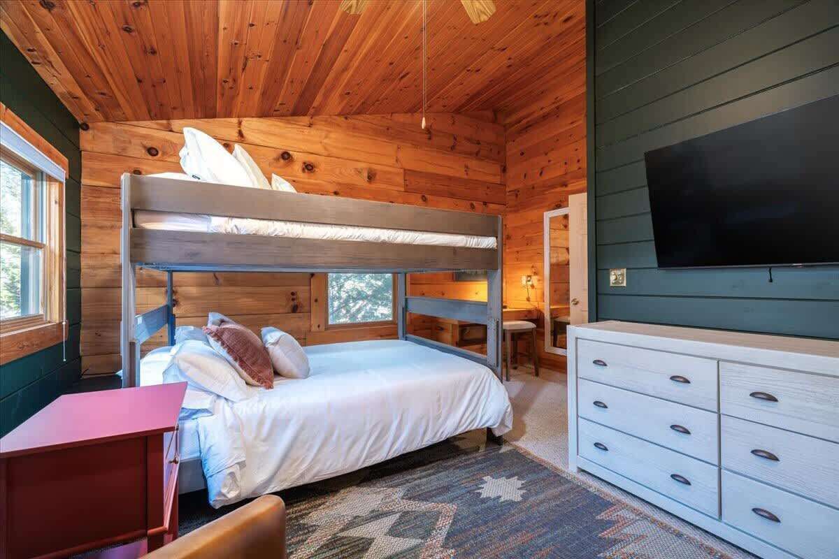 A cabin room with a bunk bed, a desk, a dresser, and a TV mounted on the wall.