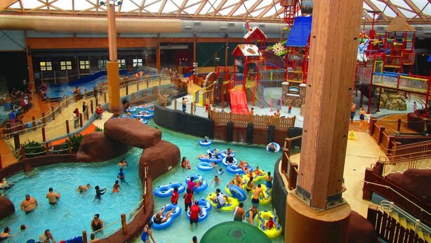 Een overdekt waterpark met meerdere zwembaden, glijbanen en speelconstructies.