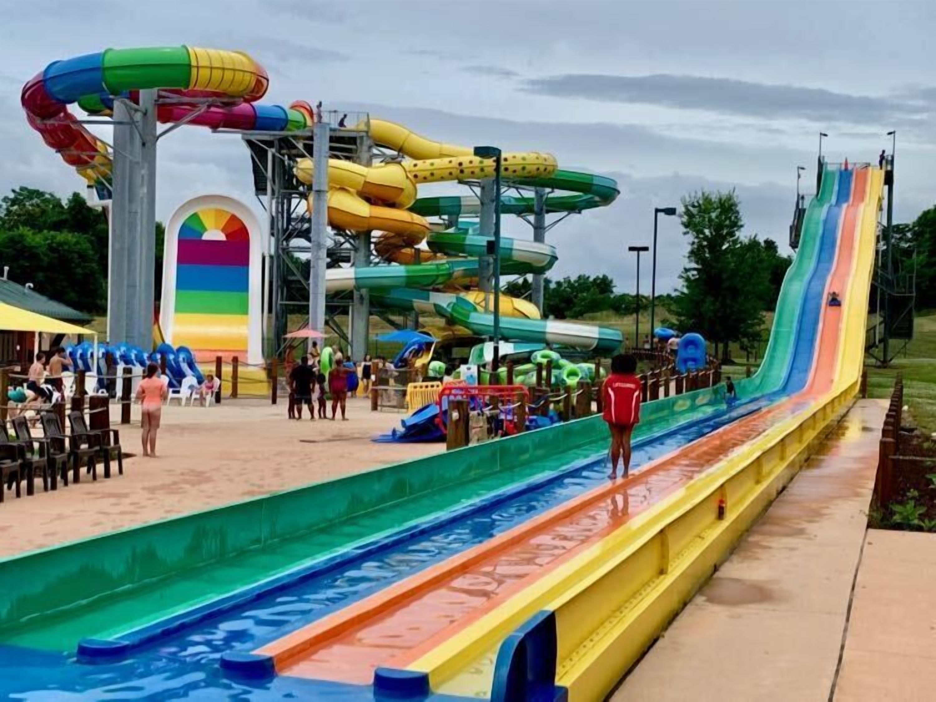 A water park with multiple water slides, a pool, and a sandy area with lounge chairs.