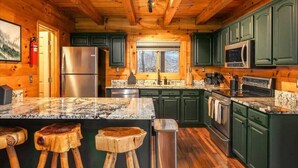 Een keuken in landhuisstijl met houten wanden, groene kastjes, een granieten aanrecht en een roestvrijstalen koelkast.