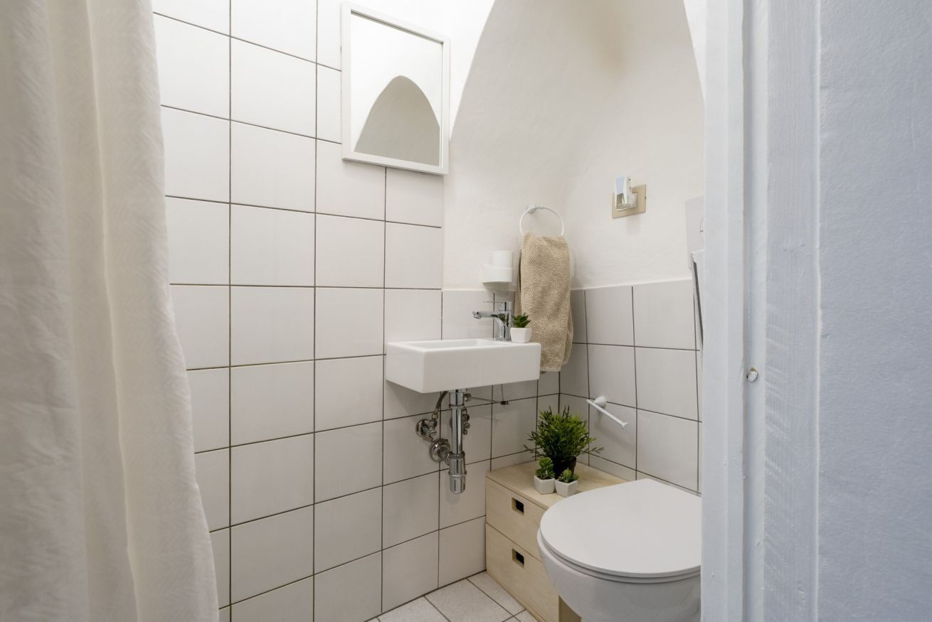 A small, white-tiled bathroom with a toilet, sink, and a mirror above it.
