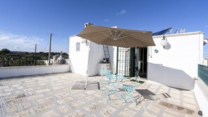 Une terrasse sur le toit, avec une table et des chaises, un grand parasol et un panneau solaire.