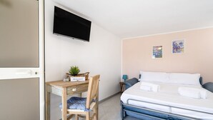 Une chambre à coucher comprenant un lit, un bureau, une chaise, un téléviseur et deux œuvres d’art accrochées au mur.