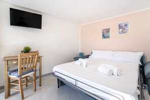 Una camera d'albergo con un letto, una scrivania, una sedia, un televisore e due opere d'arte appese alle pareti.