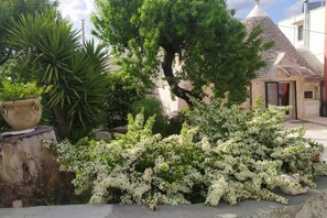 A garden with a large tree, white flowering bushes, and a stone pot.