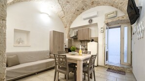 A compact living space with a dining table, chairs, a sofa, a kitchen area, and a television mounted on the wall. - GuestHost - Casa Vita 49 in Ceglie Messapica (Ceglie Messapica)