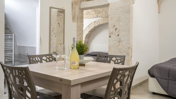 A dining area with a wooden table, six chairs, and a bottle of Santero wine. - GuestHost - Casa Vita 49 in Ceglie Messapica (Ceglie Messapica)