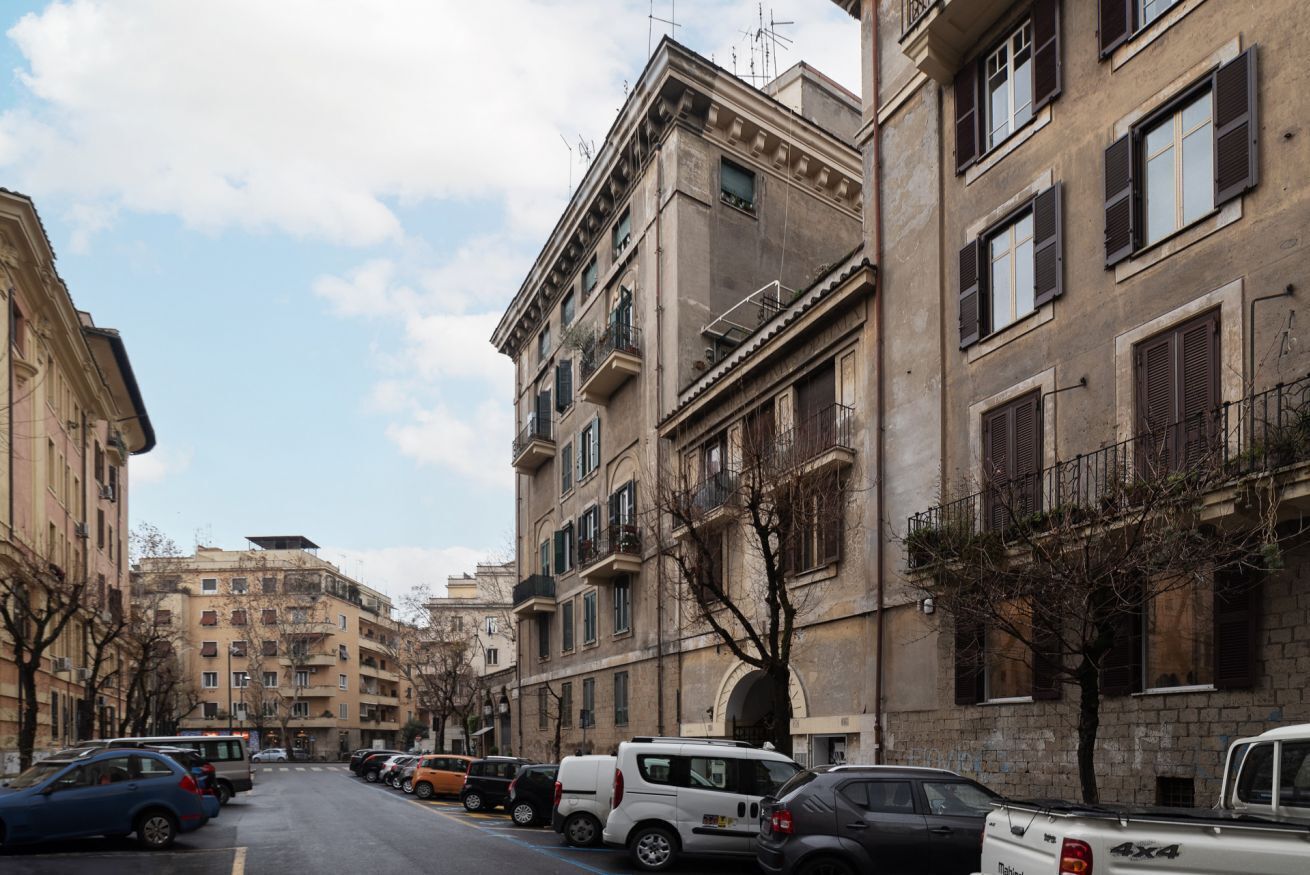 A street lined with multi-story buildings, parked cars, and trees.
