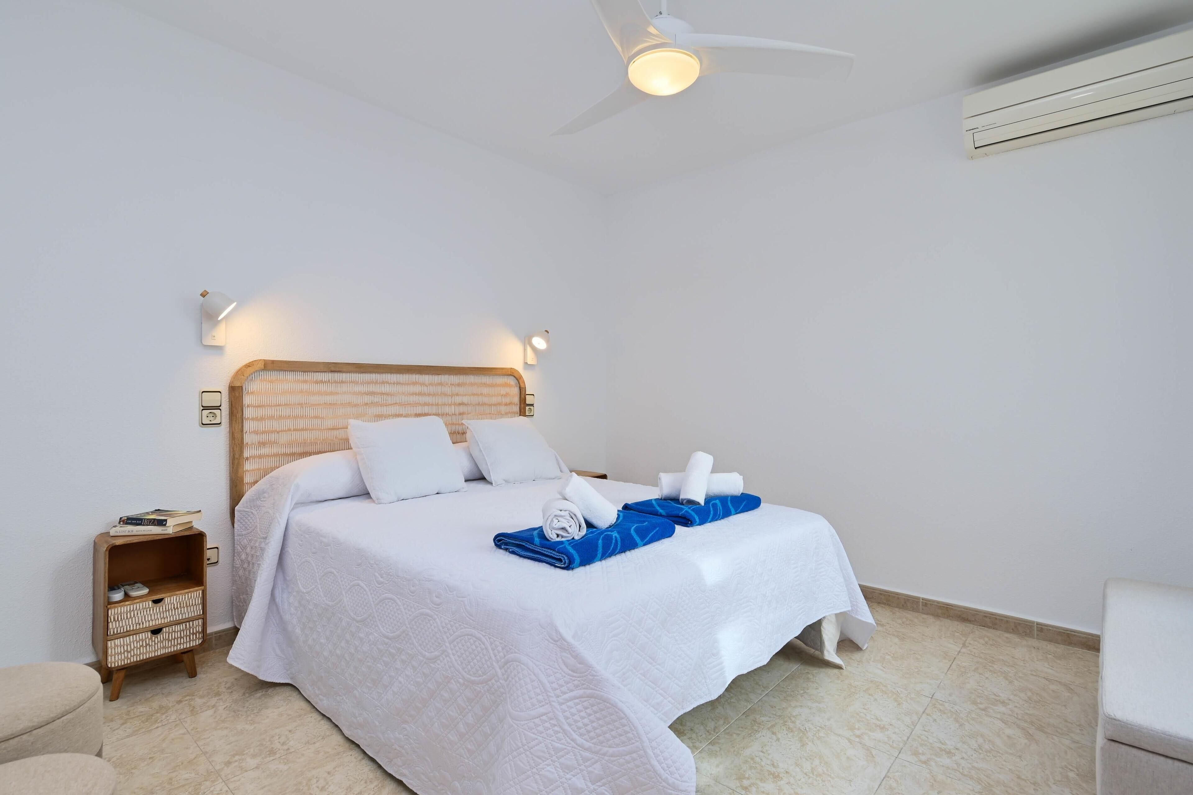 Una camera d'albergo ordinata con un letto, un comodino e una ventola a soffitto.