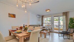A modern living room with a wooden dining table, beige chairs, a sofa, and a balcony with a view. - Wonderful and classic apartment in Javea, Costa Blanca, Spain for 4 persons (Javea)