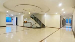 Um hall de hotel espaçoso e bem iluminado, com uma escadaria central, uma grande janela e um design de teto moderno.