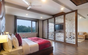 A modern hotel room with a large bed, a TV, and a balcony with decorative screens. - Hotel Royal Vrindaban  (Haridwar)