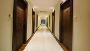 Corredor de hotel com portas de madeira, placas de quarto numeradas e piso de azulejos brilhante.