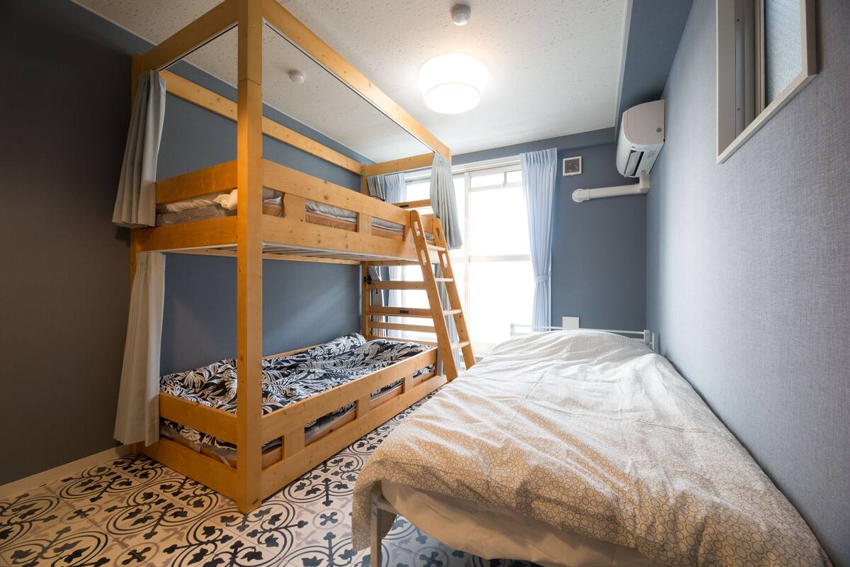 Une chambre avec un lit superposé, une échelle, une fenêtre avec des rideaux et un climatiseur fixé au mur.