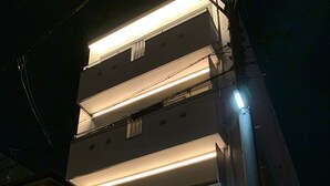 Un immeuble à plusieurs étages, doté de balcons illuminés et d’une entrée au niveau du sol.
